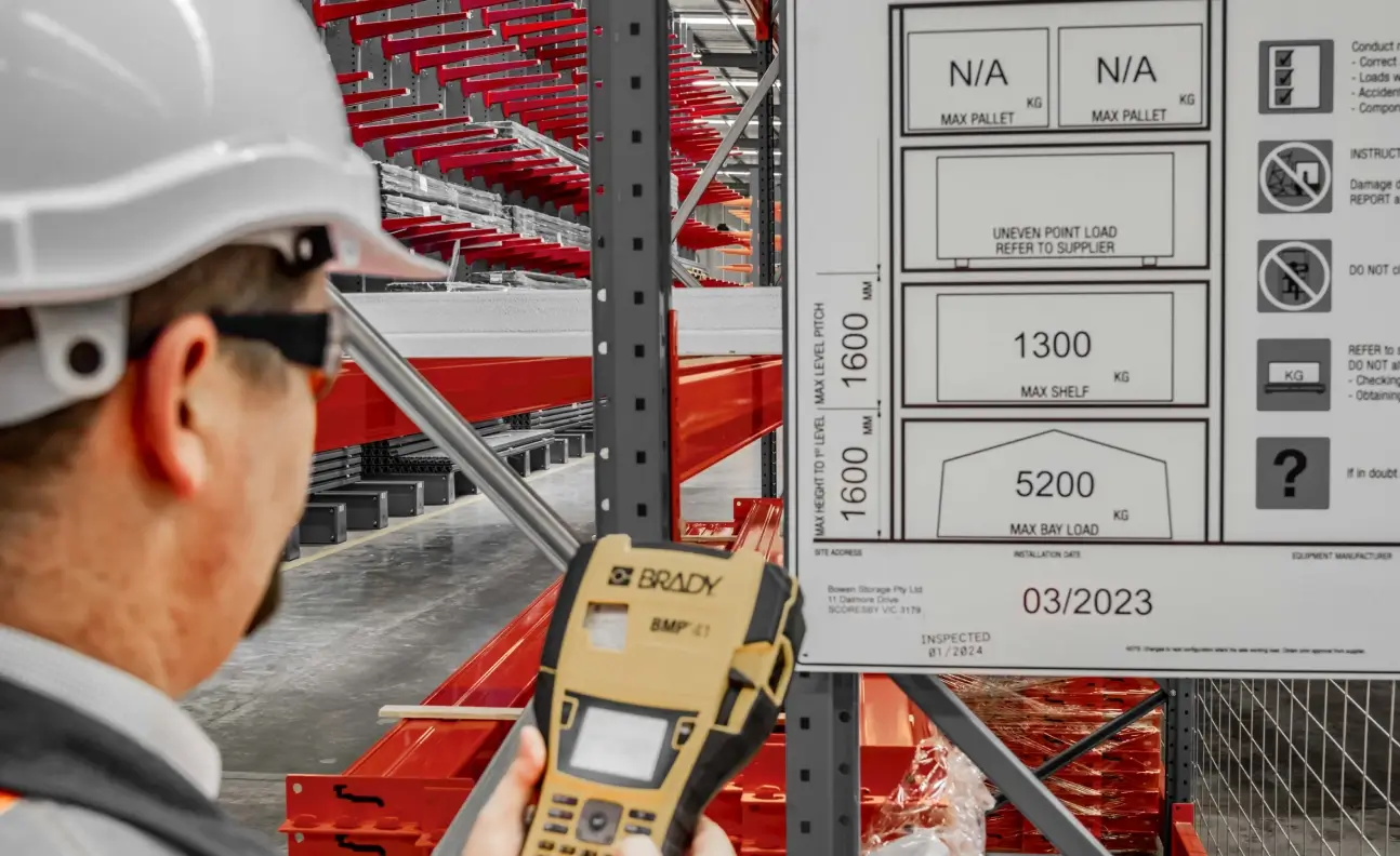 Worker verifying pallet racking load signage using handheld scanner in warehouse